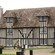 A half timbered building featuring windows, a chimney and a lawn with trees
